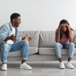 Relationship Problems Concept. Emotional annoyed stressed black couple arguing at home sitting on couch. Angry irritated nervous guy shouting at shocked and frustrated gaslighted lady, fighting